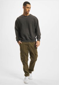 Mørkegrå sweatshirt med rund hals og ribbede manchetter, parret med olivengrønne cargo-bukser med sidelommer og elastiske manchetter, komplementeret af hvide sneakers.