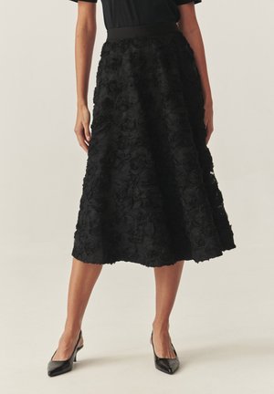 Czarna spódnica midi wykonana z teksturowanej tkaniny w kwiatowe wzory; charakteryzuje się dopasowanym paskiem w talii oraz rozkloszowanym krojem, uzupełniona o czarne szpilki.