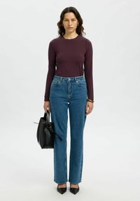 Langemouwige bordeauxrode top, high-waisted blauwe jeans, zwarte handtas en zwarte puntige hakken. Rechte pasvorm denim met lichte vervaging.
