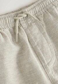 Pantalones de lino color beige claro con cintura elástica y cordón ajustable, mostrando costuras detalladas y textura del tejido.