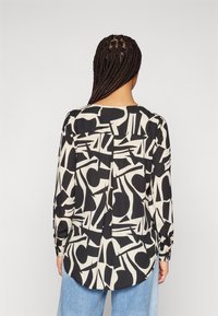 Blusa a maniche lunghe con un motivo astratto in bianco e nero, realizzata in tessuto leggero, con orlo arrotondato e dettaglio di pieghe sul retro.