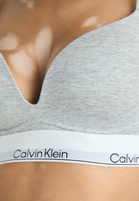 Pilkas medvilninis bevielis liemenėlė su giliu V formos iškirpimu. Yra balta juosta su juodu „Calvin Klein“ prekės ženklu. Minkšta tekstūra.