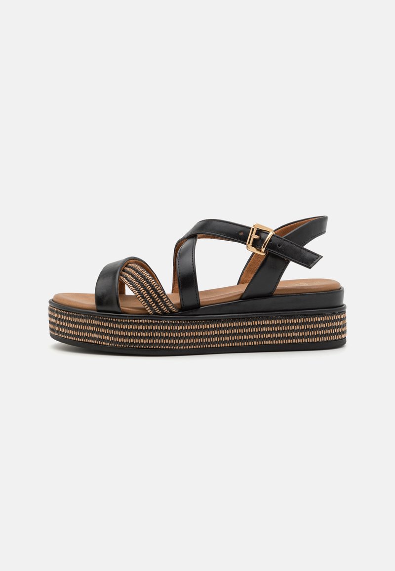 Sandales à plateforme noires avec des sangles croisées, présentant une semelle intermédiaire tissée texturée et un accent de boucle dorée. Dessus en cuir lisse et semelle intérieure beige.