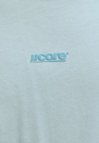 Tissu bleu clair avec logo "JJ core" en relief brodé dans un bleu légèrement plus foncé centré sur la surface.