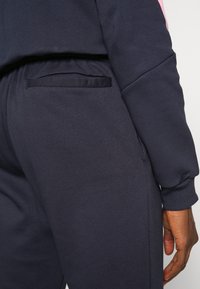 Pantalones deportivos de color azul marino en material suave, con un bolsillo horizontal en el lado derecho y una silueta ajustada con puño elástico.