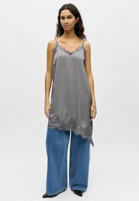 Camisole en satin gris avec bordure en dentelle, dotée de fines bretelles et d'une forme fluide, associée à un jean en denim bleu à jambes larges.