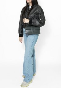Giacca bomber in pelle nera, jeans svasati azzurri chiari e borsa a tracolla grigia con design piatto e dettagli di cucitura. Sneakers testurizzate.