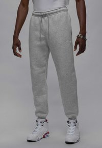 Grå fleece joggingbukser med elastisk talje og snøre, med et lille broderet logo og tætsiddende manchetter, parret med hvide høje sneakers.