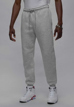 Gray fleece joggers with elastic waistband and drawstring, featuring a small embroidered logo and tapered cuffs, paired with white high-top sneakers.