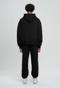 Zwarte oversized hoodie en bijpassende joggingbroek, gemaakt van zachte stof met geribbelde manchetten, gedragen met witte sneakers.