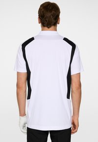 Vit polo-shirt med svarta sidodetaljer och korta ärmar, med krage och en mjuk, blandad tygkvalitet.