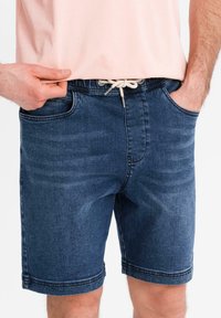 Shorts en jean de couleur bleu foncé avec une coupe décontractée. Comprend des poches avant, une taille à cordon de serrage et des ourlets cousus pour plus de durabilité.