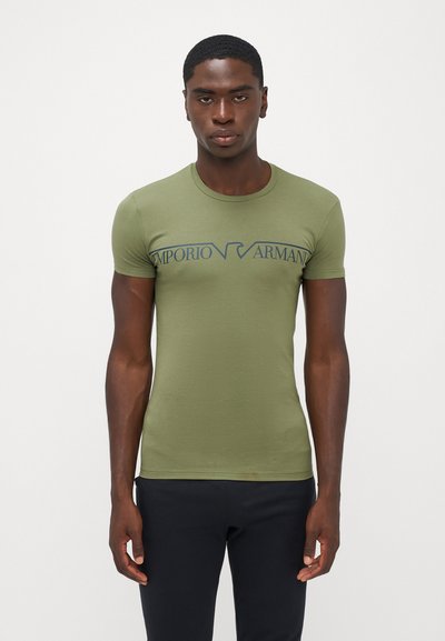 Tricou scurt pe mâneci, de culoare verde măSlin, cu un design ajustat, prezentând un logo al Emporio Armani, de culoare albastră, pe piept. Textură netedă, asemănătoare cu bumbacul.