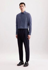 Marineblauw shirt met lange mouwen en een stippenpatroon, gecombineerd met donkere formele broek en zwarte schoenen, gepresenteerd op een neutrale achtergrond.