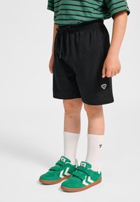 Svarta atletiska shorts med dragsko i midjan. Matchas med gröna sneakers med vita detaljer och vita, ribbade crew-strumpor.