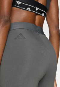 Sivé legíny s vystúpeným logom Adidas, bezšvovým dizajnom a elastickým pásom s kontrastným čiernym pruhom s logom.