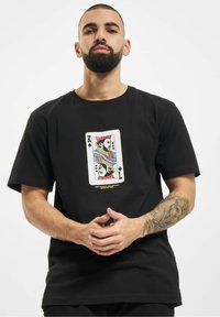 Black short-sleeve t-shirt featuring a colorful king of spades playing card graphic at the center with text below in yellow.