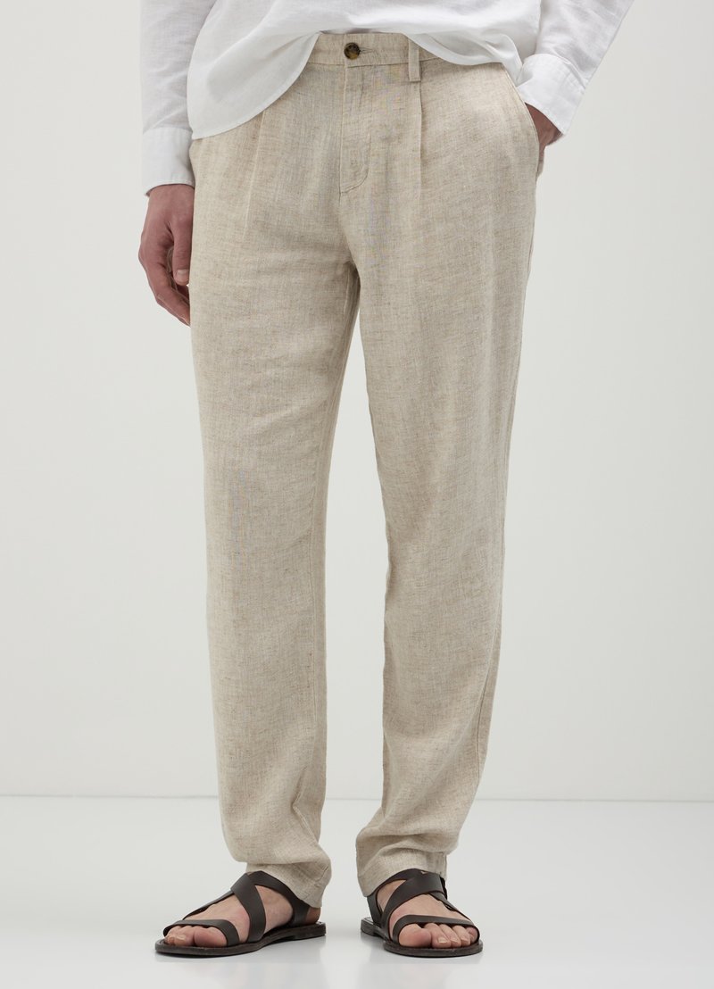 Pantalon en lin beige avec une finition texturée, présentant un pli avant unique, des poches latérales et une fermeture à bouton. Porté avec des sandales foncées.