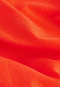 Tessuto liscio arancione brillante con trama a maglia fine visibile e pieghe delicate che creano ombre morbide.