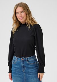 Black long-sleeve top with textured fabric, high ruffled collar, and gathered cuffs, paired with a blue denim skirt and belt.