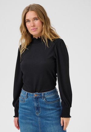 Haut noir à manches longues en tissu texturé, avec un col froncé haut et des poignets froncés, associé à une jupe en denim bleu et une ceinture.