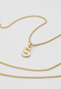 Goldene Halskette mit einer verdrehten Kette, die einen auffälligen, glänzenden, kursiven "S"-Anhänger in poliertem Finish zeigt.