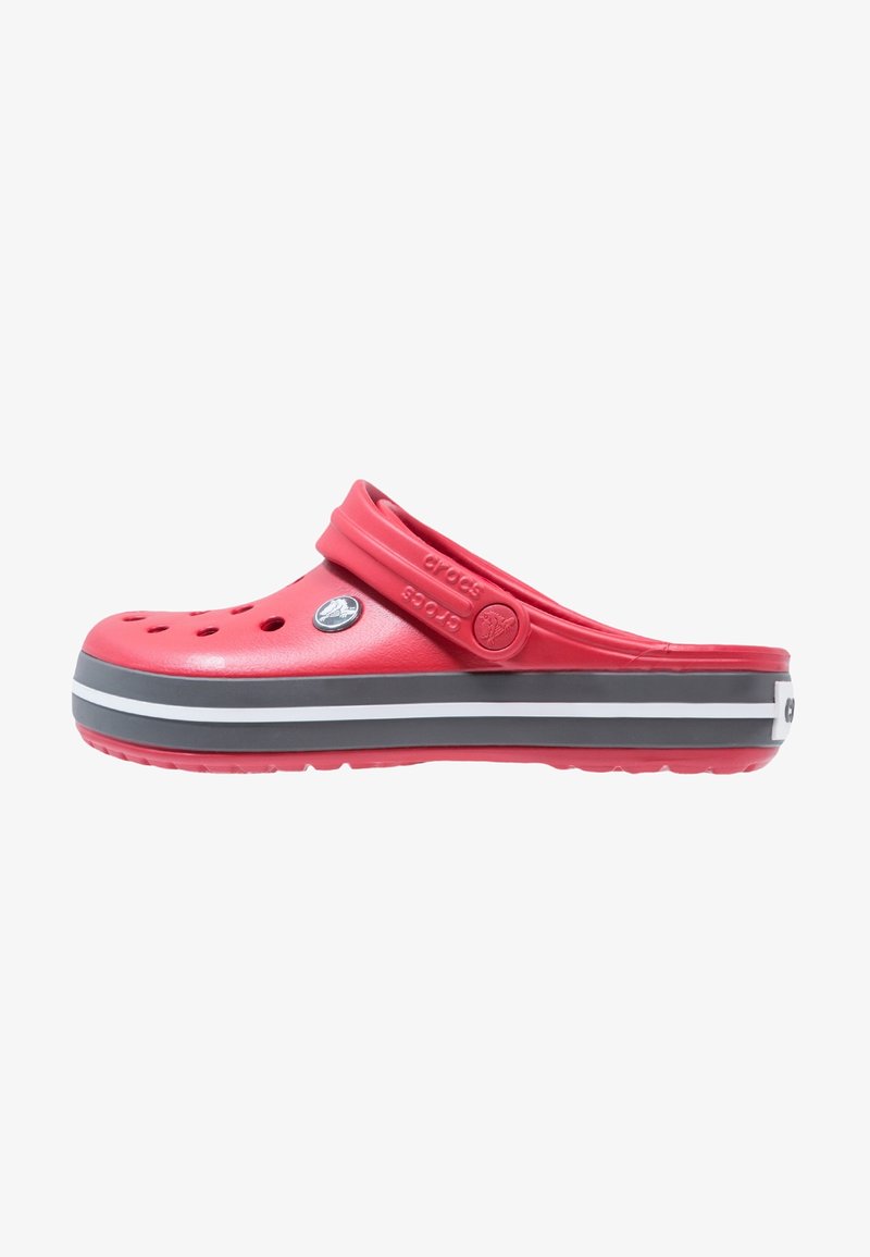 Zueco de goma roja con orificios de ventilación, una correa ancha y una suela a rayas grises y blancas. Textura suave con un acabado brillante.