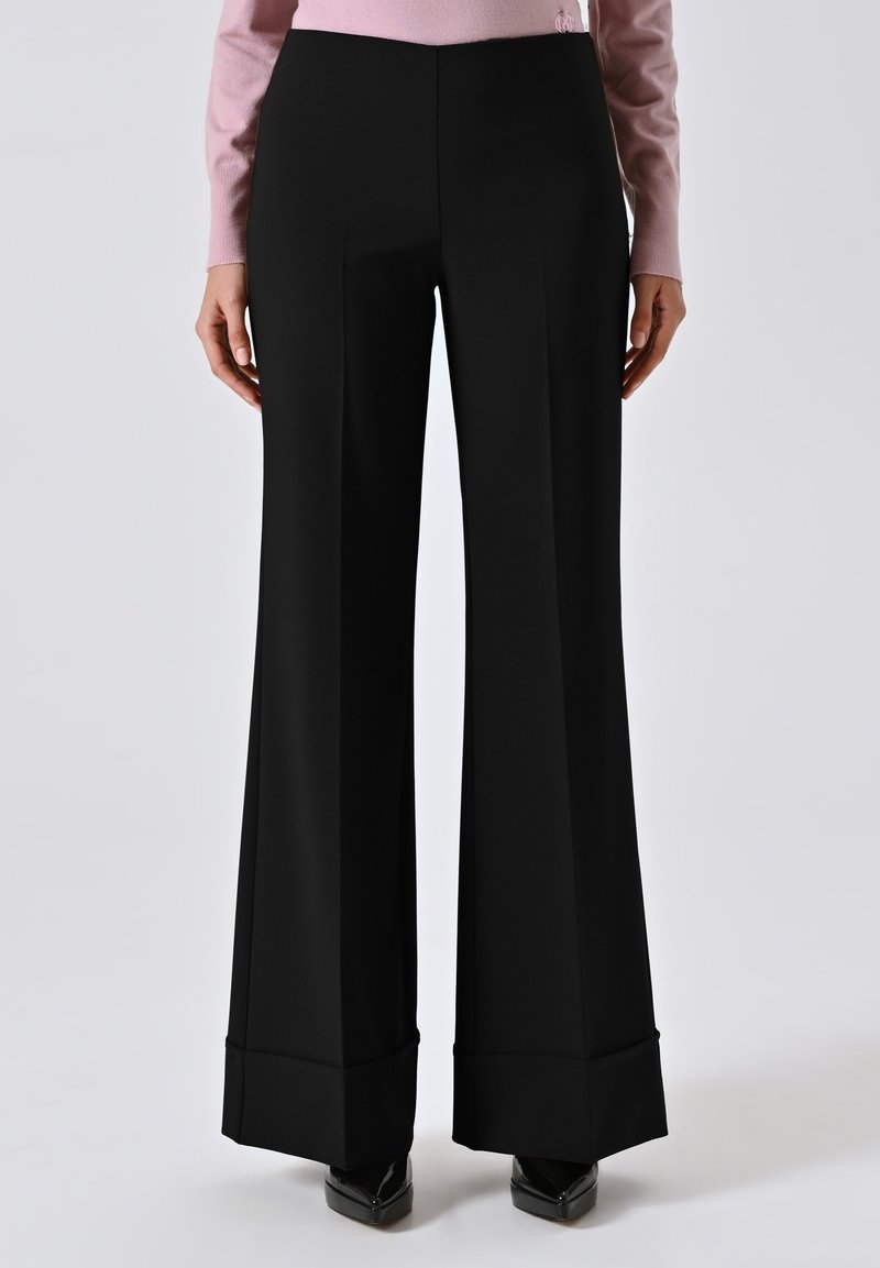 Pantaloni neri a gamba larga realizzati in un tessuto liscio, con una vestibilità su misura e orli piegati. Abbinati a scarpe con tacco alto per un look formale.