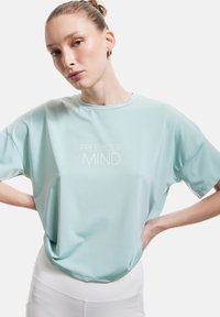 Camiseta atlética de manga corta en azul claro, fabricada con tejido que absorbe la humedad, con el texto "LIBERA TU MENTE" en blanco centrado en el frente.