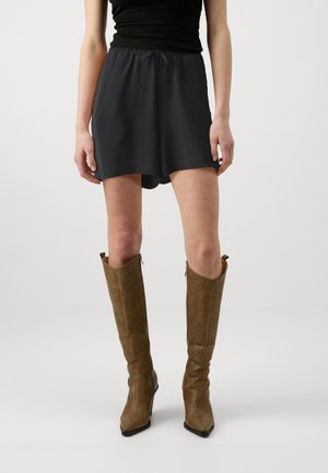 Black, lightweight skirt with an elastic waistband. Paired with knee-high, brown leather boots featuring a pointed toe and decorative stitching.