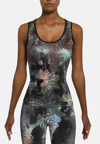 Kobieta w bezrękawniku i legginsach w abstrakcyjny wzór o kolorach czarnym, szarym, niebieskim i różowym przedstawiający dmuchawce.