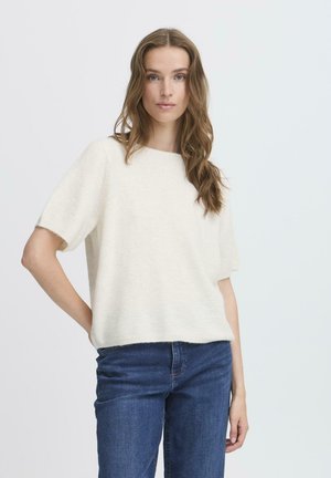 Lichtcrème korte mouwen trui met een zachte textuur en een rechte snit, gedragen met donkerblauwe jeans, handen in de zakken.