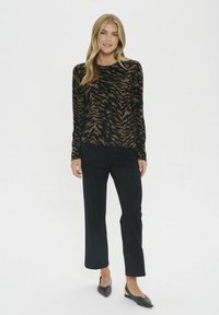 Mustega varrukaga topp musta ja pruuni tiigri triibu mustris, koos mustade sirgete pükste ja mustade teravate ninaga kingadega.