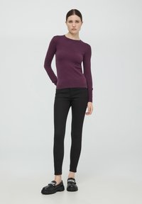 Maglione a maniche lunghe color bordeaux in tessuto morbido, abbinato a pantaloni neri attillati. Scarpe basse con suola spessa e dettaglio in catena argentata.