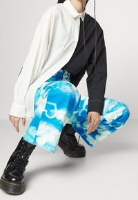 Musta ja valkoinen pitkähihainen paita nappilista, yhdistettynä sinisiin pilvikuvioisiin housuihin ja mustiin nauhakenkiin, joissa on paksu pohja.