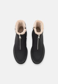 Zwarte leren enkellaarzen met een zachte, beige bontvoering. Voorzien van een zilveren ritssluiting aan de voorkant en een afgeronde neus.