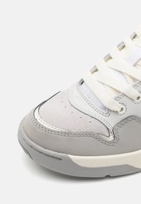 Lys grå sneaker med en glat læder-overdel, teksturerede suede-detaljer, cremefarvede snørebånd og en gummisål. Rundet tå med syningdetaljer.