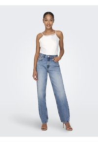 Camiseta blanca sin mangas con tirantes finos, combinada con unos jeans de mezclilla de corte ancho y cintura alta de color azul claro. Modelo con tacones beige.