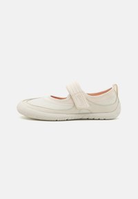 Scarpa slip-on beige con punta arrotondata, cinturino elastico texturizzato, fodera morbida e suola in gomma flessibile con dettagli antiscivolo.