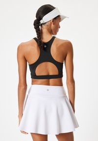Svart sportbh med utskärningsdesign och slät textur, kombinerad med en vit utsvängd kjol som har logodetalj och elastisk midja.