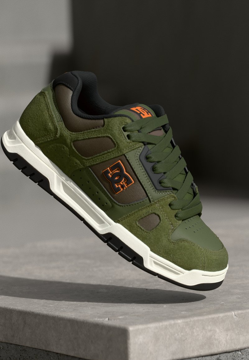 Green suede skate shoes with black accents, featuring a textured upper, padded collar, and a white rubber sole. Logo displayed in orange.