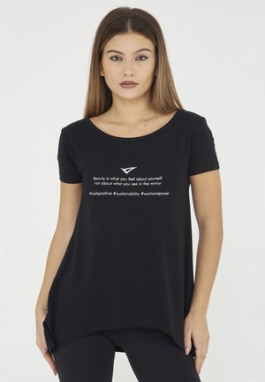 Giovane donna con capelli lisci che indossa una maglietta nera con la scritta "La bellezza è quello che senti di te stessa, non quello che vedi nello specchio."