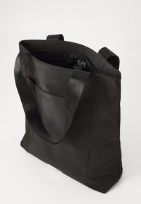 Borsa tote nera con una texture liscia, ampio interno, doppi manici in tessuto e una tasca frontale. Marchio visibile all'interno.