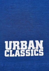 Mėlynas medvilninis marškinėlis su tekstu "URBAN CLASSICS" didelėmis baltomis raidėmis. Lygus paviršius, įprastas kirpimas ir be papildomų grafikų.