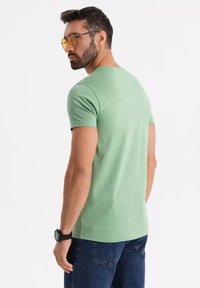 Zelené tričko s krátkým rukávem z měkké bavlny, s klasickým kruhovým výstřihem a slim fit, kombinované s tmavými džíny a černými hodinkami.