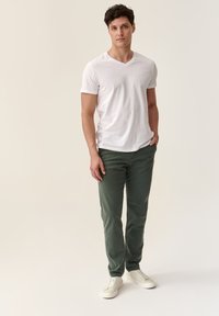 Camiseta blanca de cuello en V, pantalones verdes de corte recto, zapatillas blancas. Diseño sencillo, tejido ligero y un ajuste relajado. Sin patrones notables.