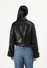 Veste en cuir noir à motif crocodile avec un design court, des manches larges et un détail de ceinture, associée à un jean bleu taille haute.