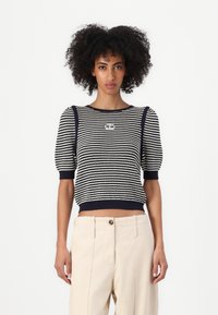 Maglione corto a righe blu navy e bianche lavorato a maglia con maniche a sbuffo e scollo rotondo. Presenta un dettaglio del logo sul davanti e orlo a coste.