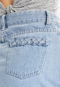 Jean en denim bleu clair avec un accent tressé sur la poche arrière. Le tissu a une texture douce et un design classique à cinq poches.