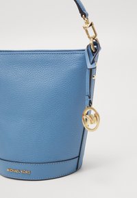 Borsa a secchiello in pelle blu con superficie testurizzata, hardware dorato e pendente con logo. Caratterizzata da una tracolla removibile e nome del marchio impresso.